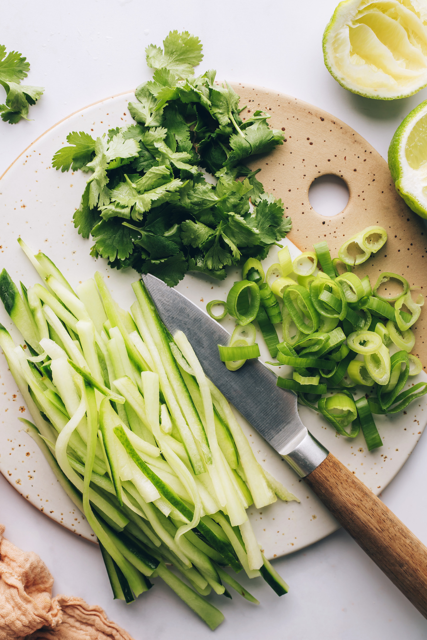 Limes next to a cutting board with cucumbers, green onion, and cilantro