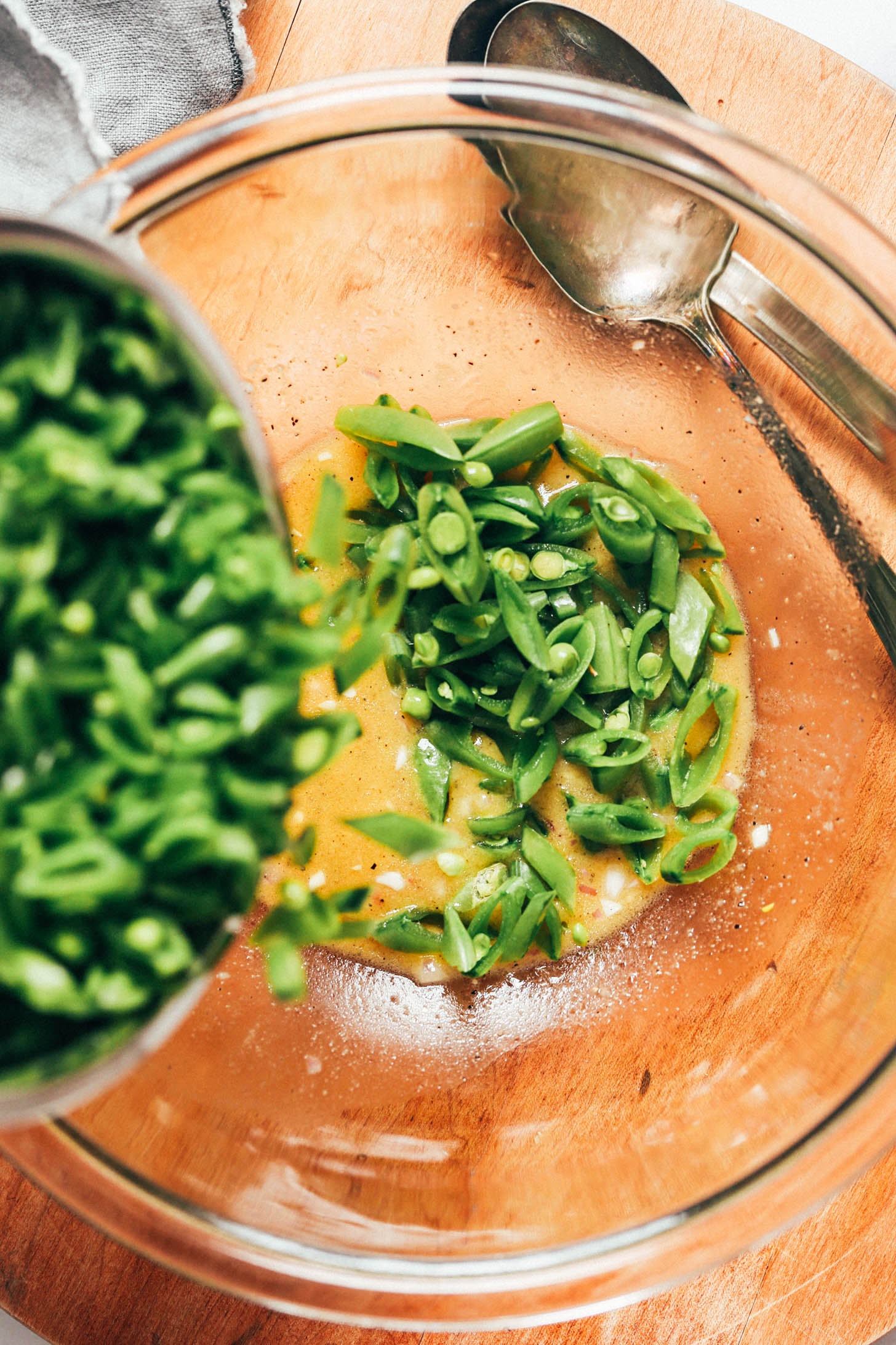 Pouring sliced snap peas into a bowl of lemon mustard vinaigrette
