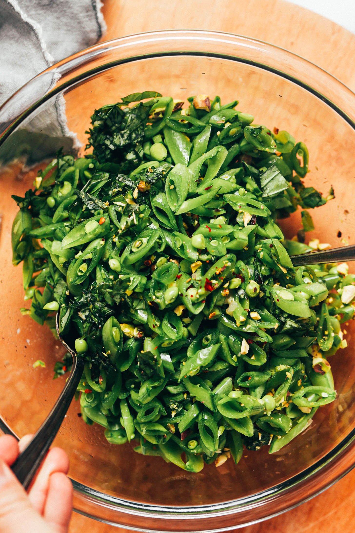 Using serving spoons to toss the snap pea salad with dressing