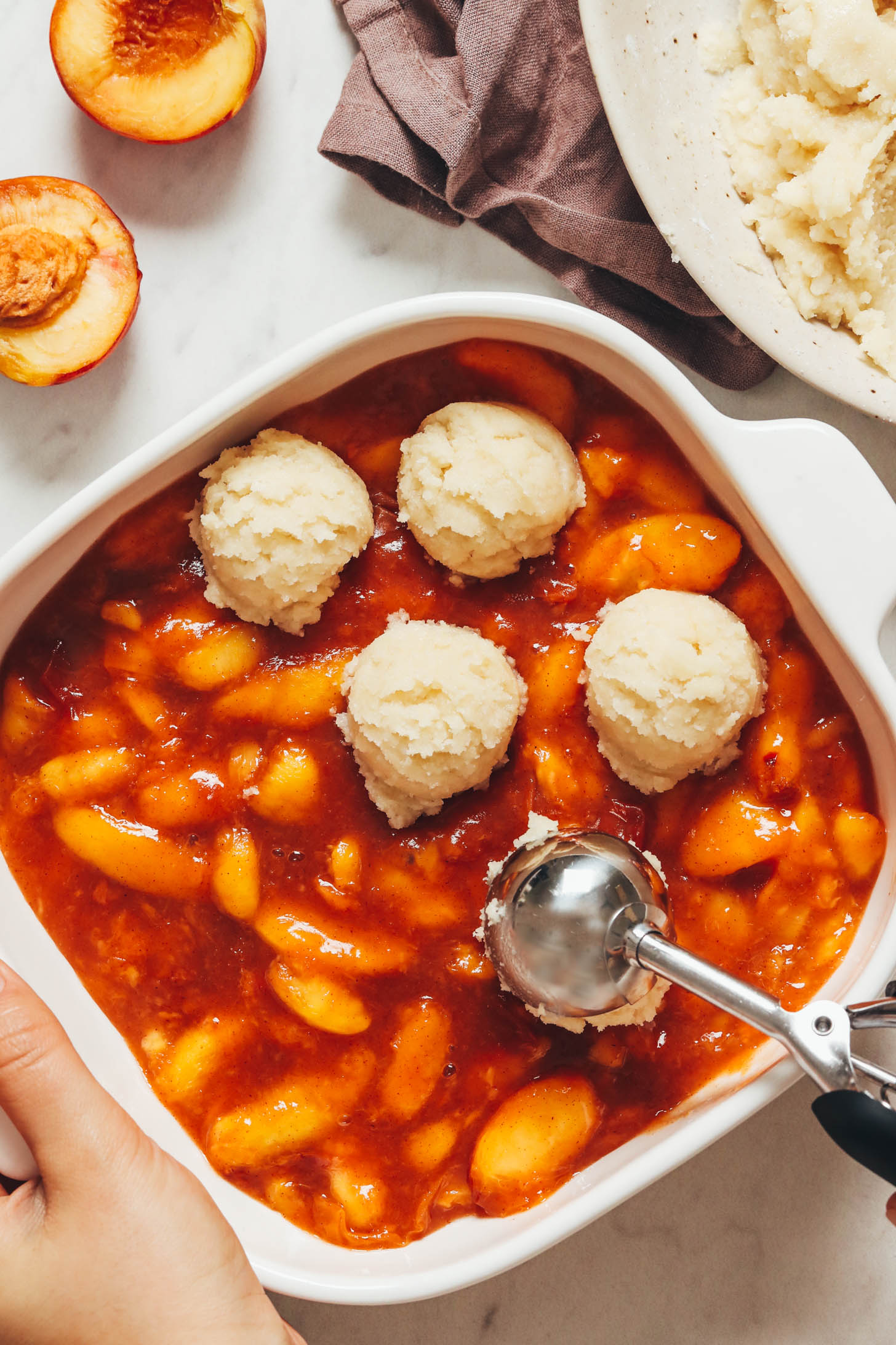 Using a small cookie scoop to add gluten-free biscuits over a peach filling