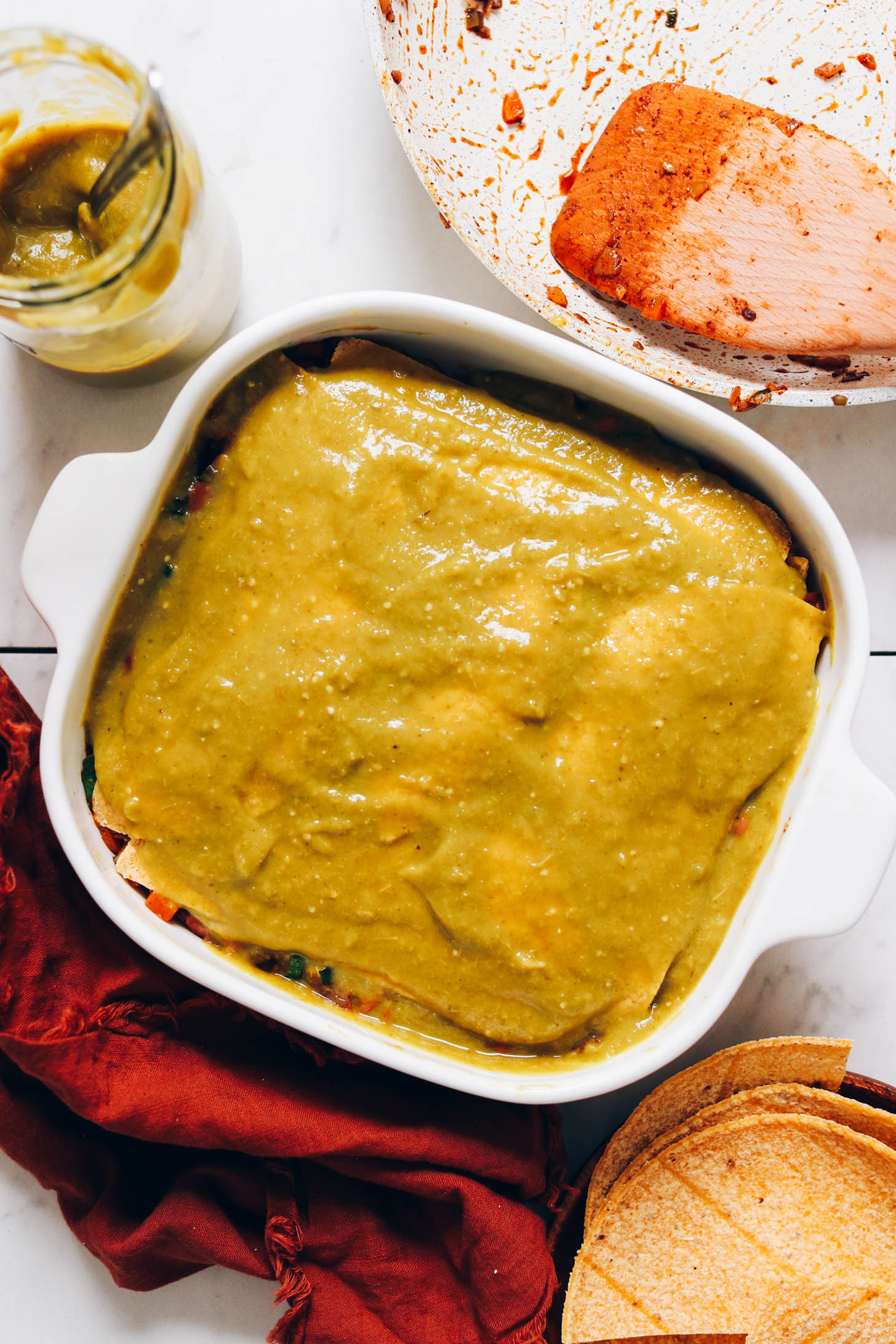 Baking pan showing green enchilada sauce over layers of tortillas and filling