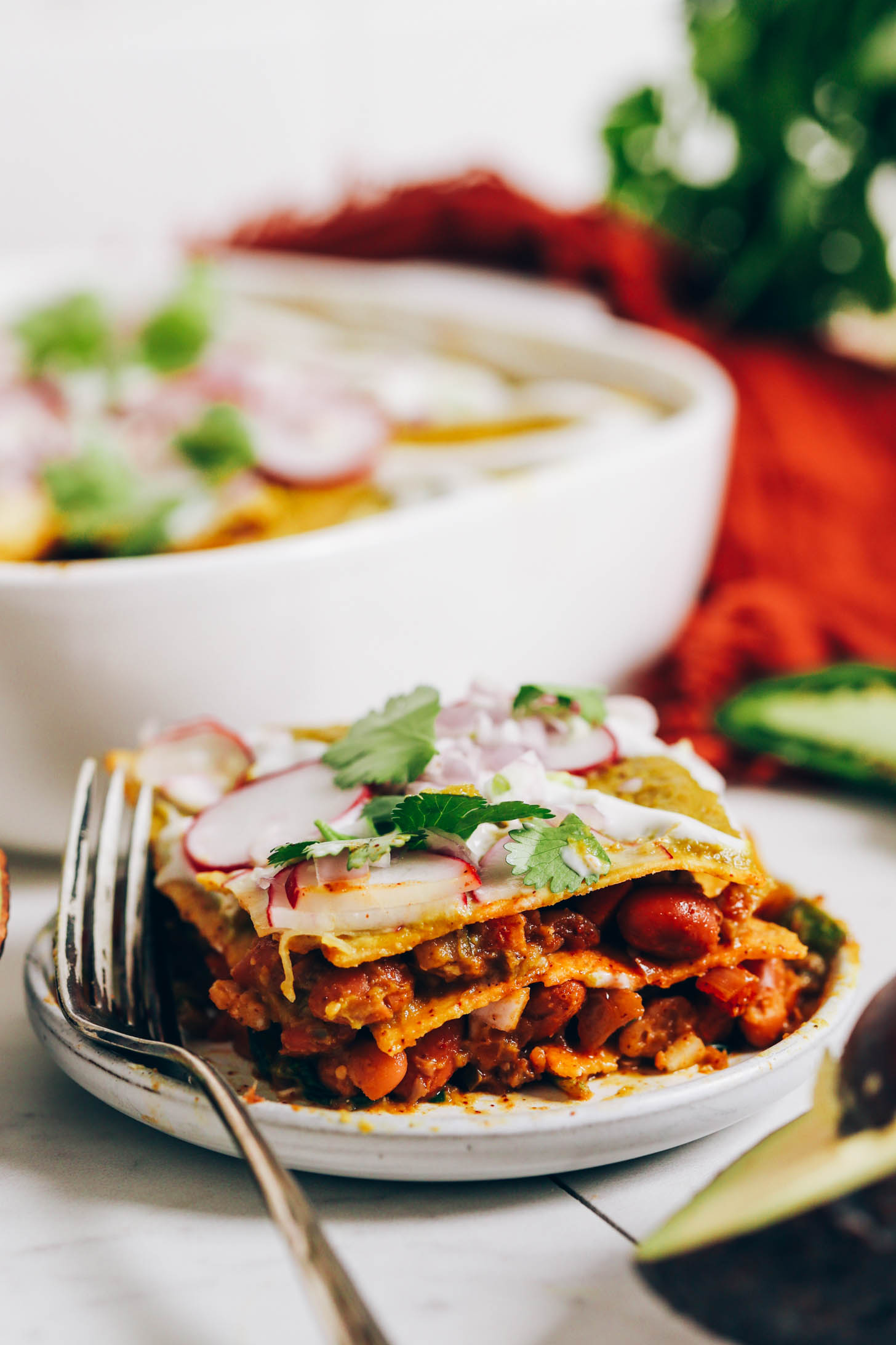 Plate with a layered enchilada bake topped with cilantro, vegan sour cream, radish, and shallot