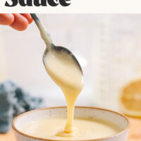 Homemade vegan hollandaise sauce dripping from a spoon into a bowl