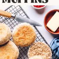 Jam and butter next to a cooling rack of gluten-free English muffins with text that says tender and crusty