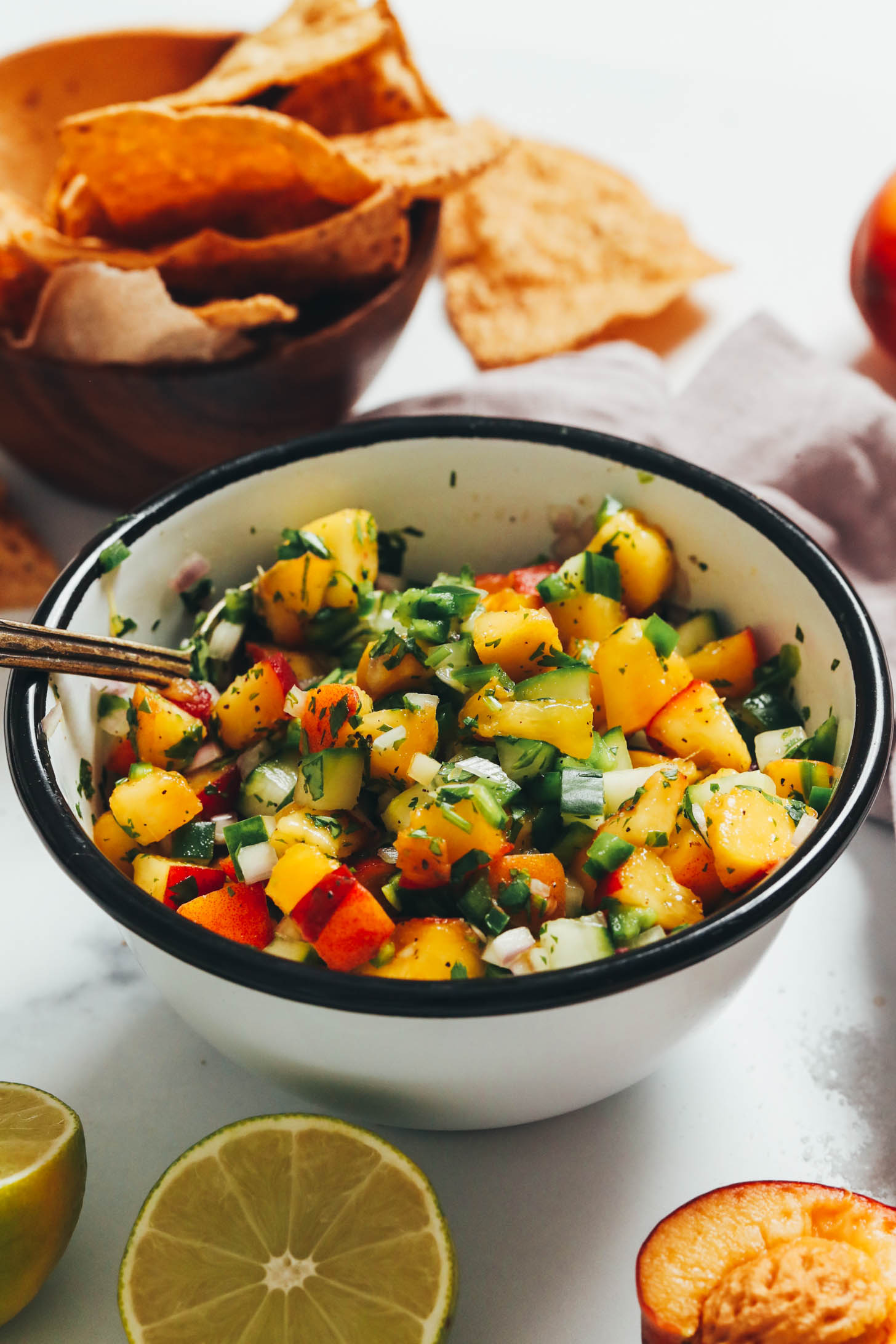 Tortilla chips next to a bowl of peach cucumber salsa