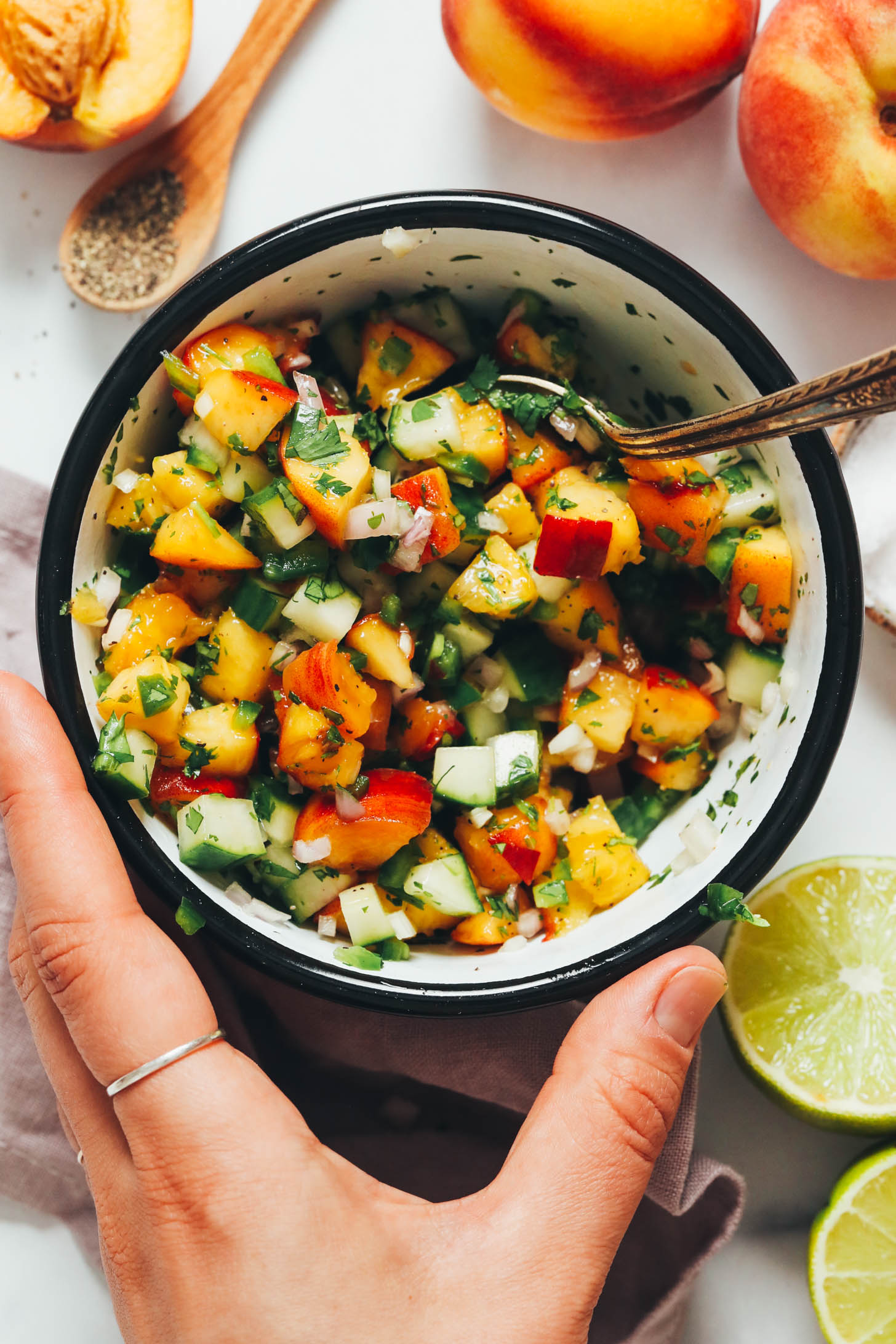 Peaches, limes, and black pepper around a bowl of fresh peach salsa