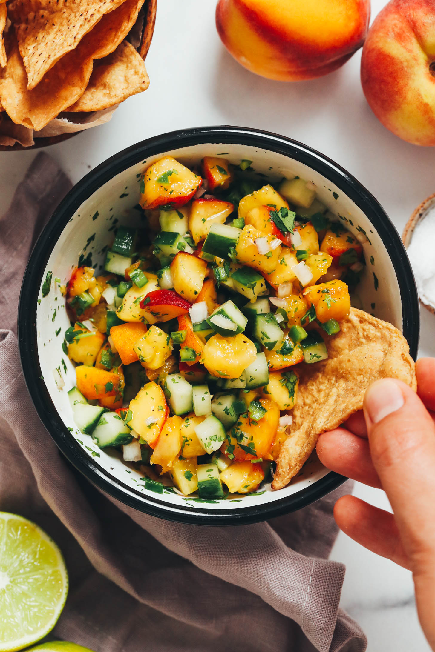 Dipping a tortilla chip into a bowl of peach cucumber salsa