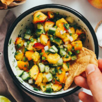 Dipping a tortilla chip into a bowl of peach salsa