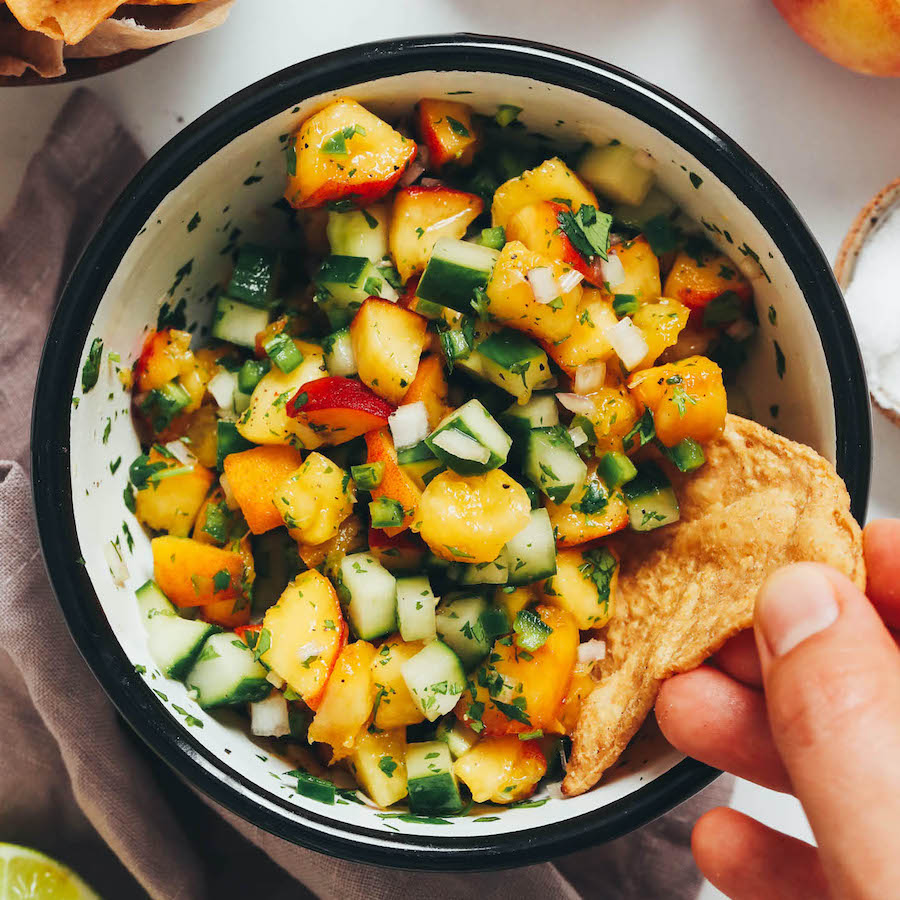 Dipping a tortilla chip into a bowl of peach salsa