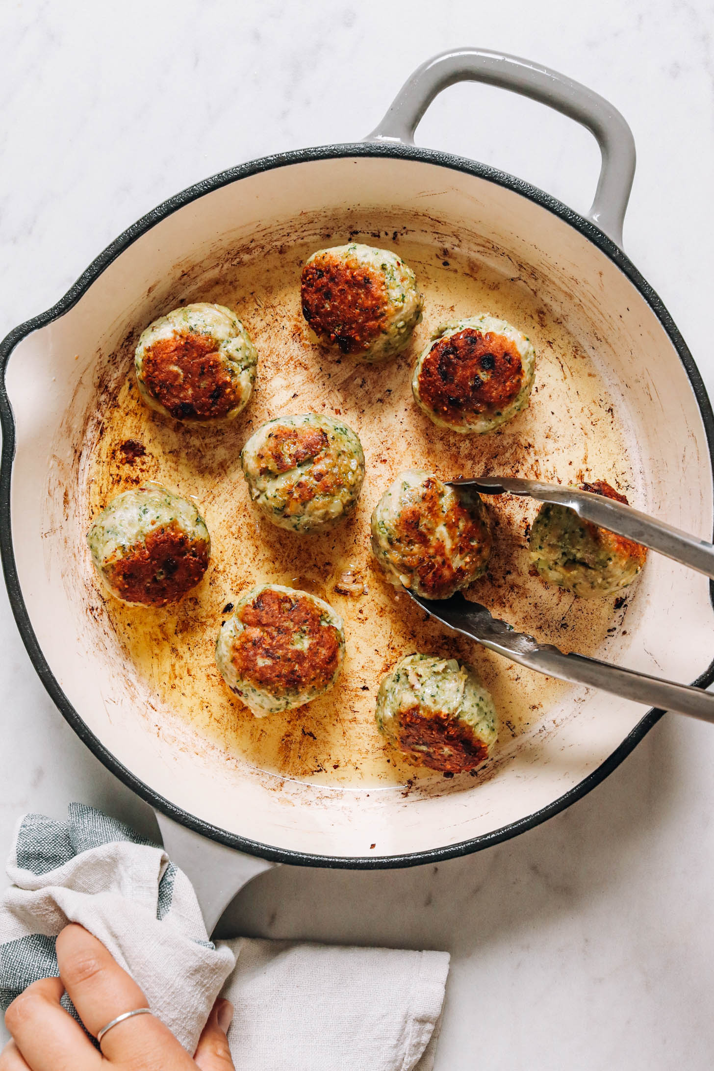 Using metal tongs to flip a turkey meatball in a skillet