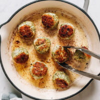 Using metal tongs to flip a turkey meatball cooking in a skillet