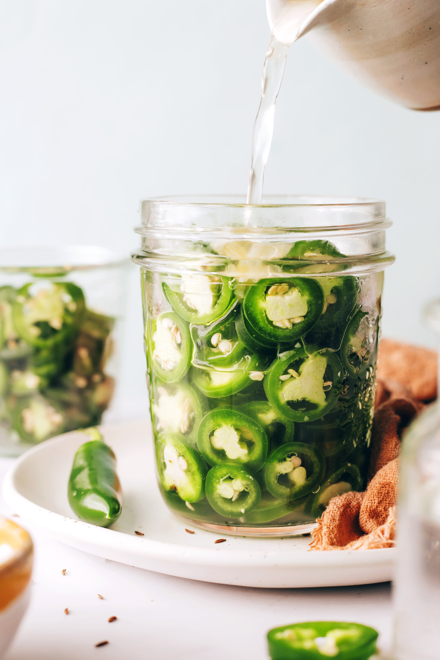 Pouring a warm vinegar brine over sliced jalapenos
