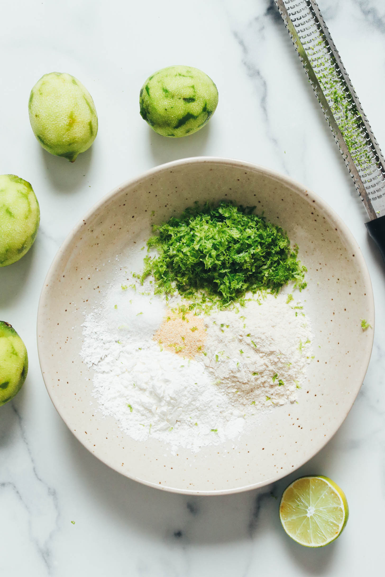 Zested limes around a bowl of lime zest, brown rice flour, garlic powder, salt, and corn starch