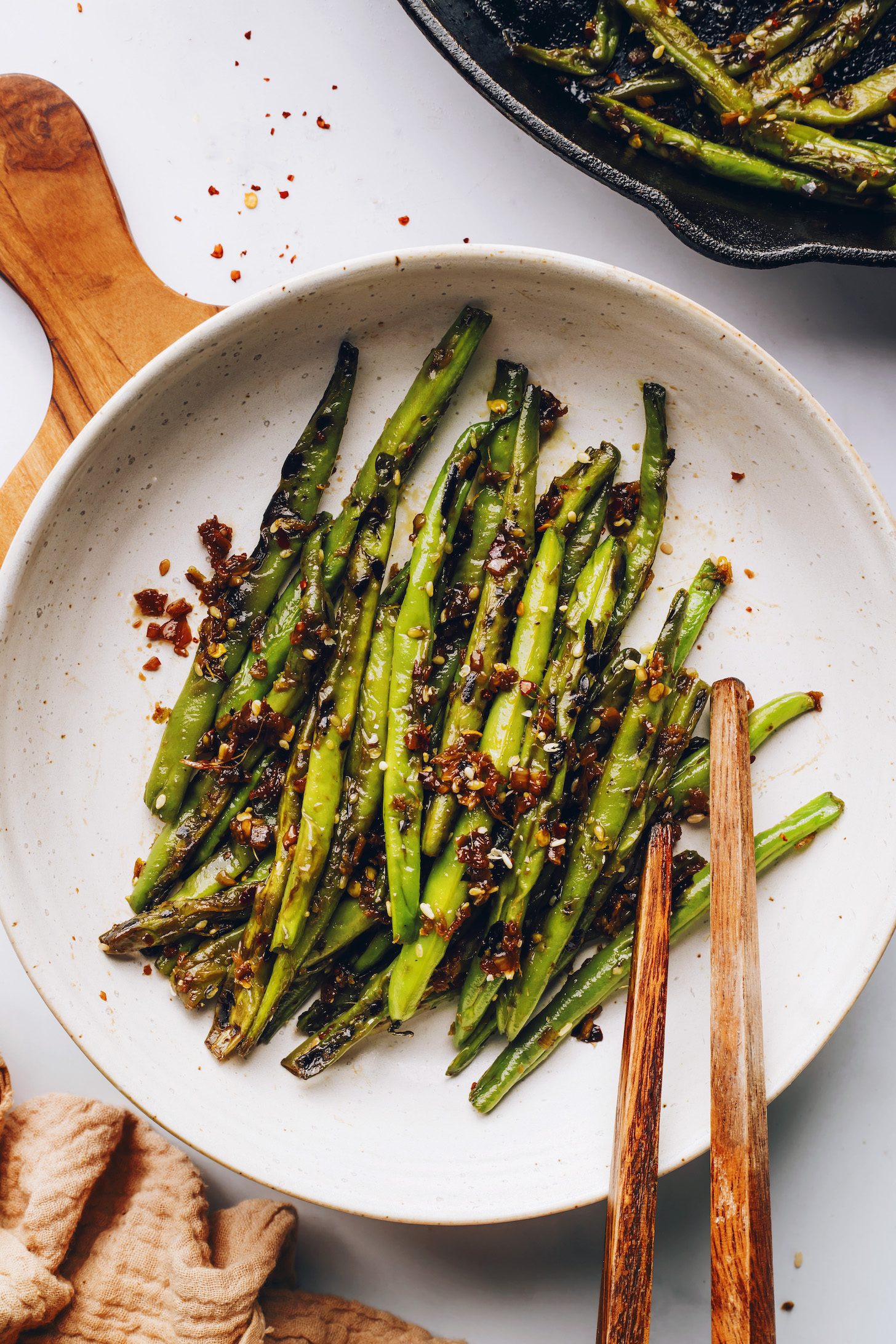Chopsticks reaching in to grab stir fried green beans from a plate