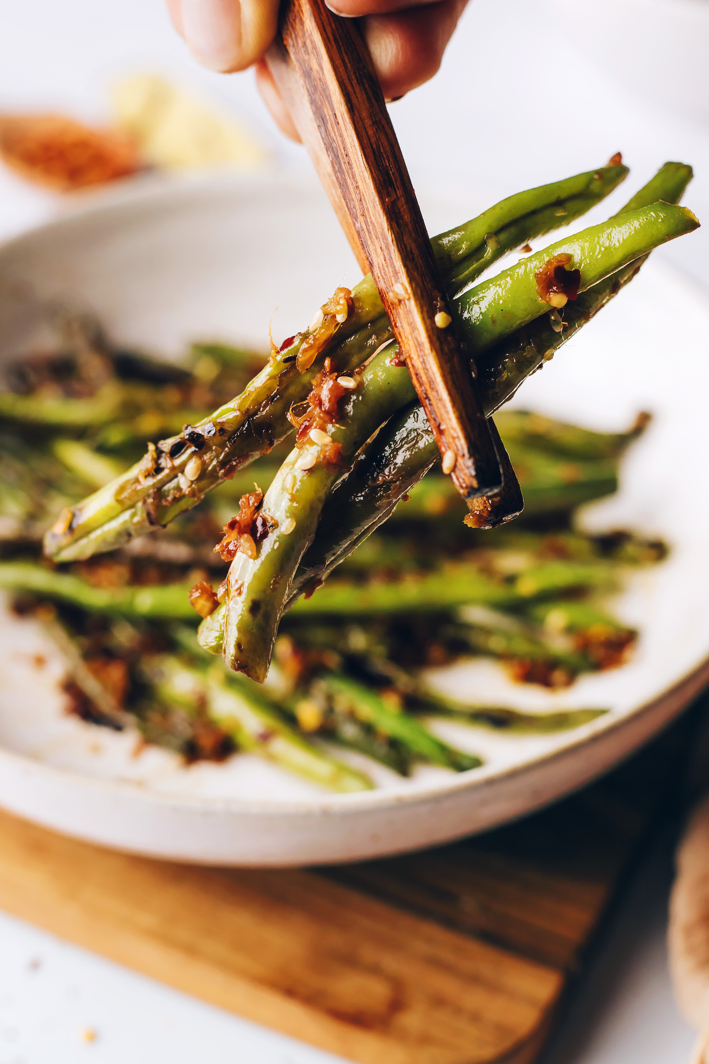 Chopsticks holding a bite of spicy garlicky green beans next to a bowl