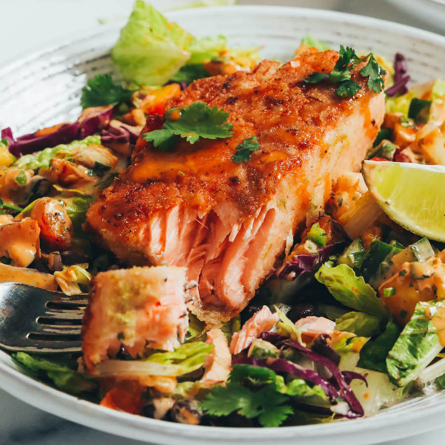 Bite of flaky salmon on a fork next to a smoky salmon salad