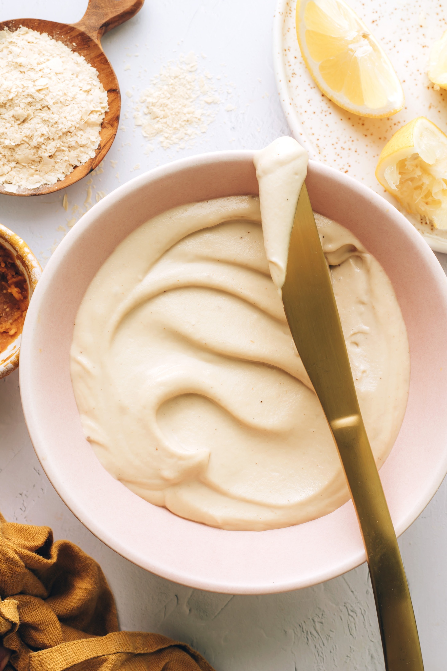 Nutritional yeast, miso paste, and lemon wedges around a bowl of homemade vegan cream cheese