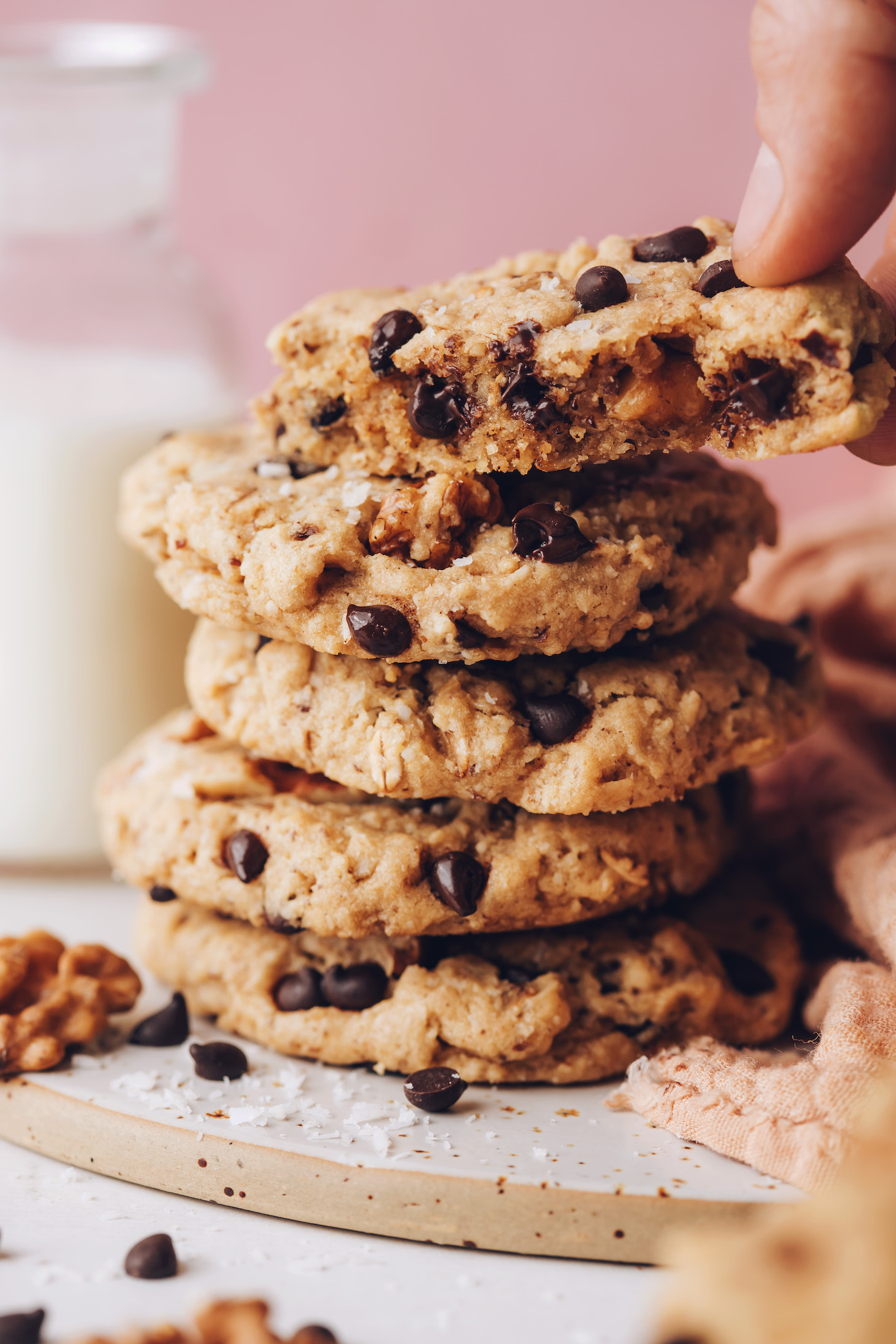 Hand reaching in to pick up a partially eaten cowgirl cookie from a stack of more cookies