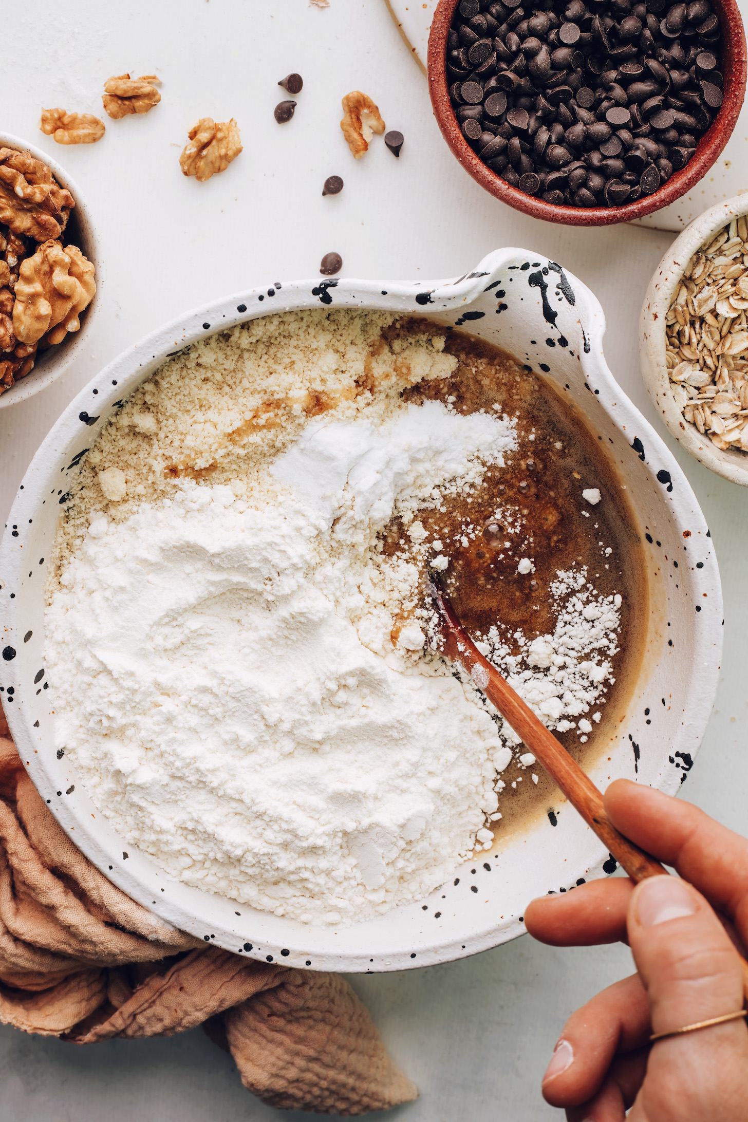 Using a wooden spoon to stir almond flour and gluten-free flour blend into the wet ingredients