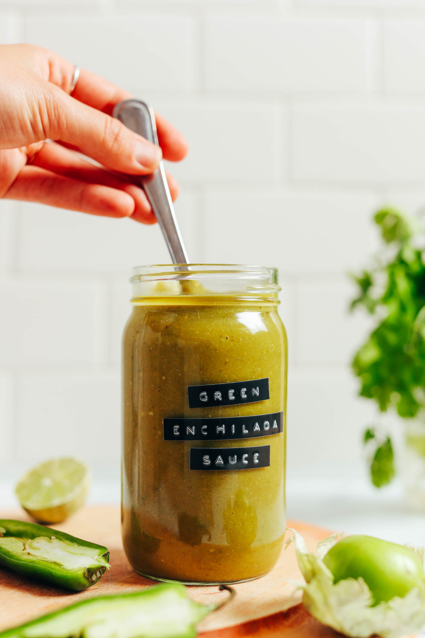 Jalapeños, tomatillo, lime, and cilantro next to a jar of green enchilada sauce