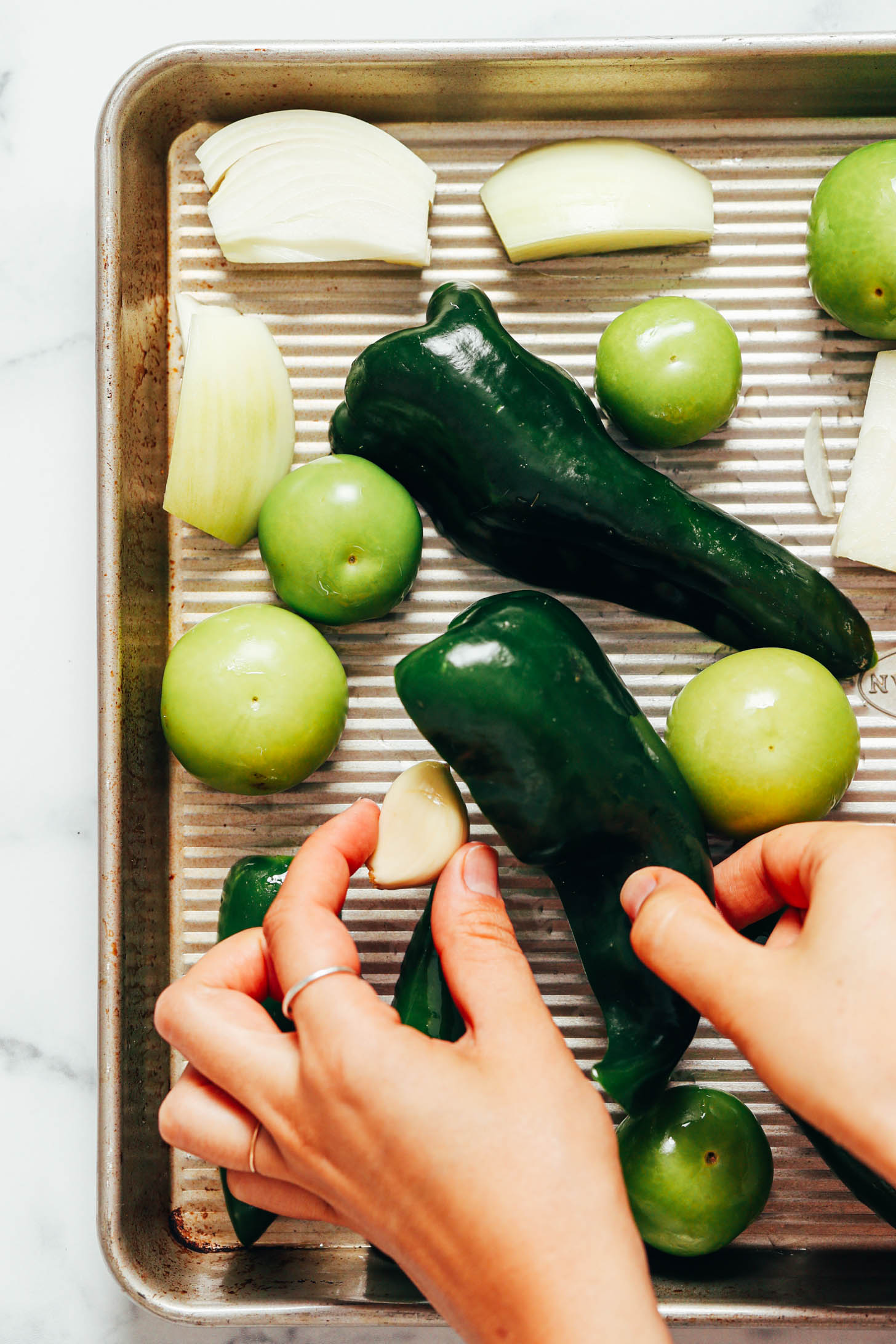 Placing garlic and a poblano pepper on a baking sheet next to tomatillos and onions