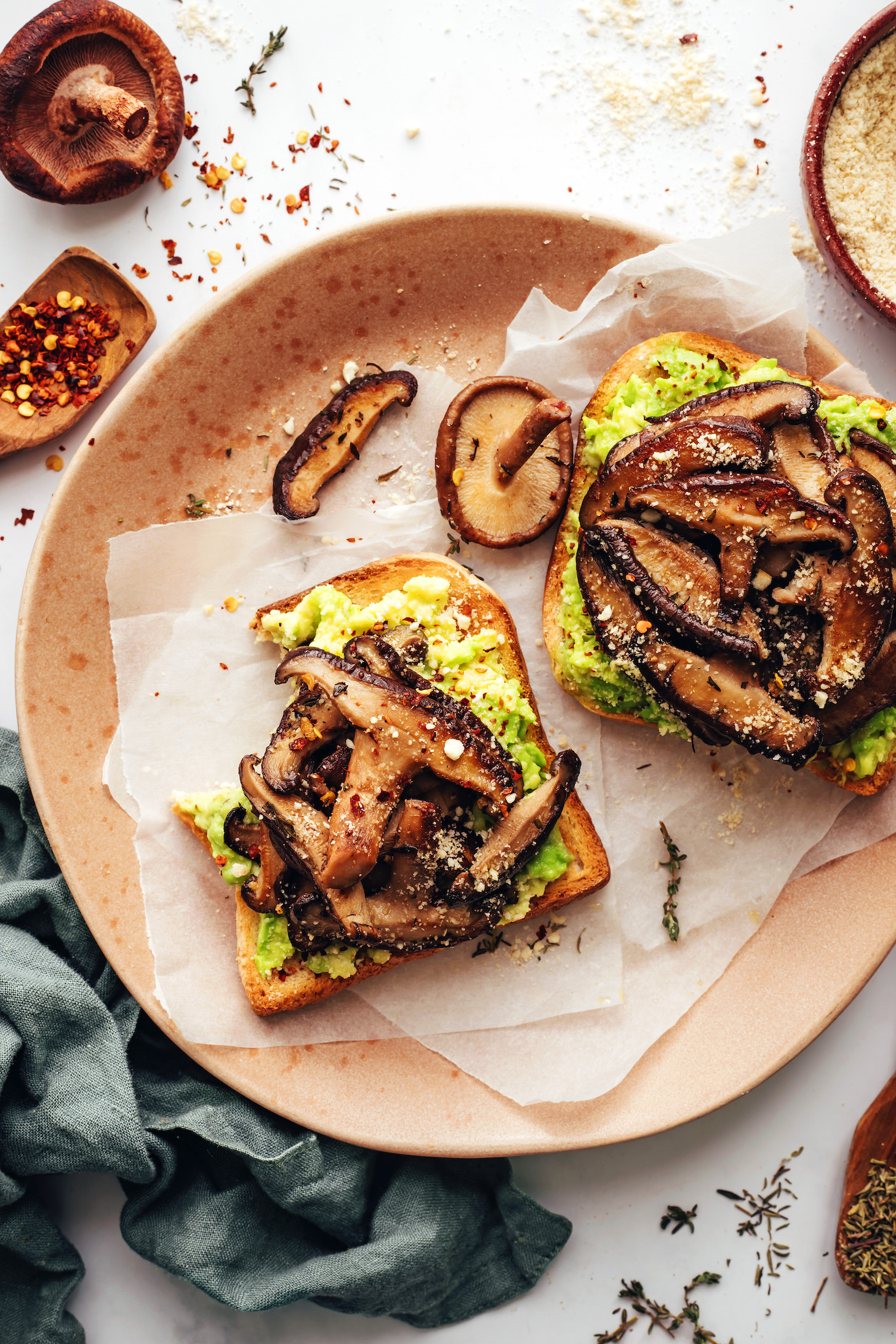 Plate with two slices of mushroom avocado toast topped with red pepper flakes and vegan parmesan