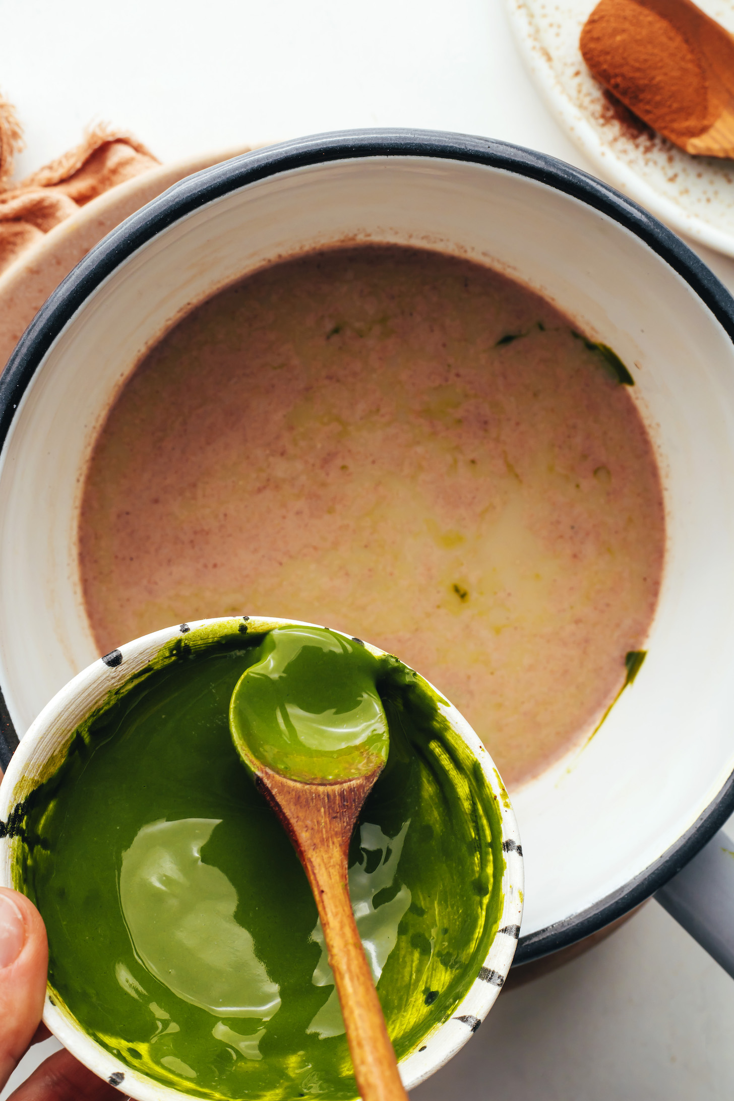 Pouring dissolved matcha powder into a saucepan of dairy-free milk and sweetener