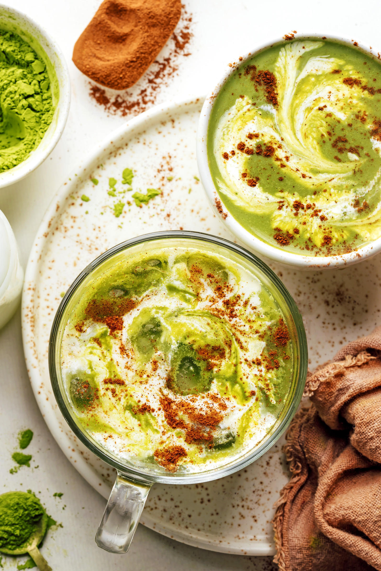 Matcha powder and pumpkin pie spice next to mugs of our iced and hot pumpkin spice matcha latte recipe