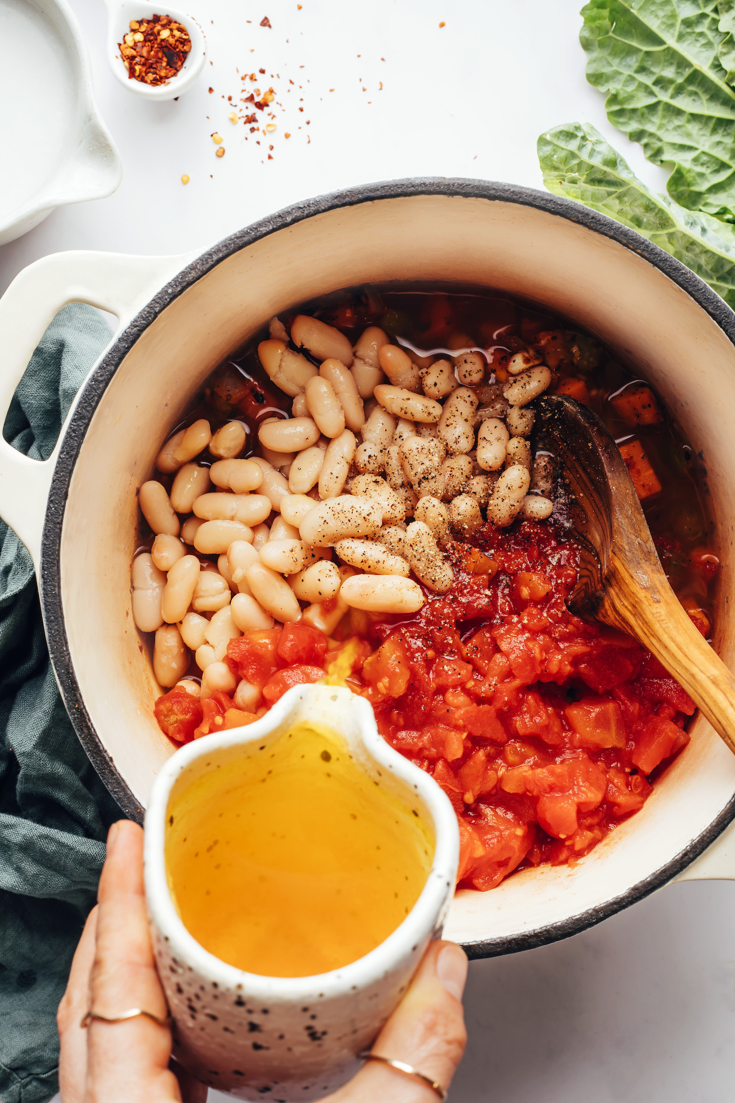 Adding vegetable broth to a pot with white beans and diced tomatoes
