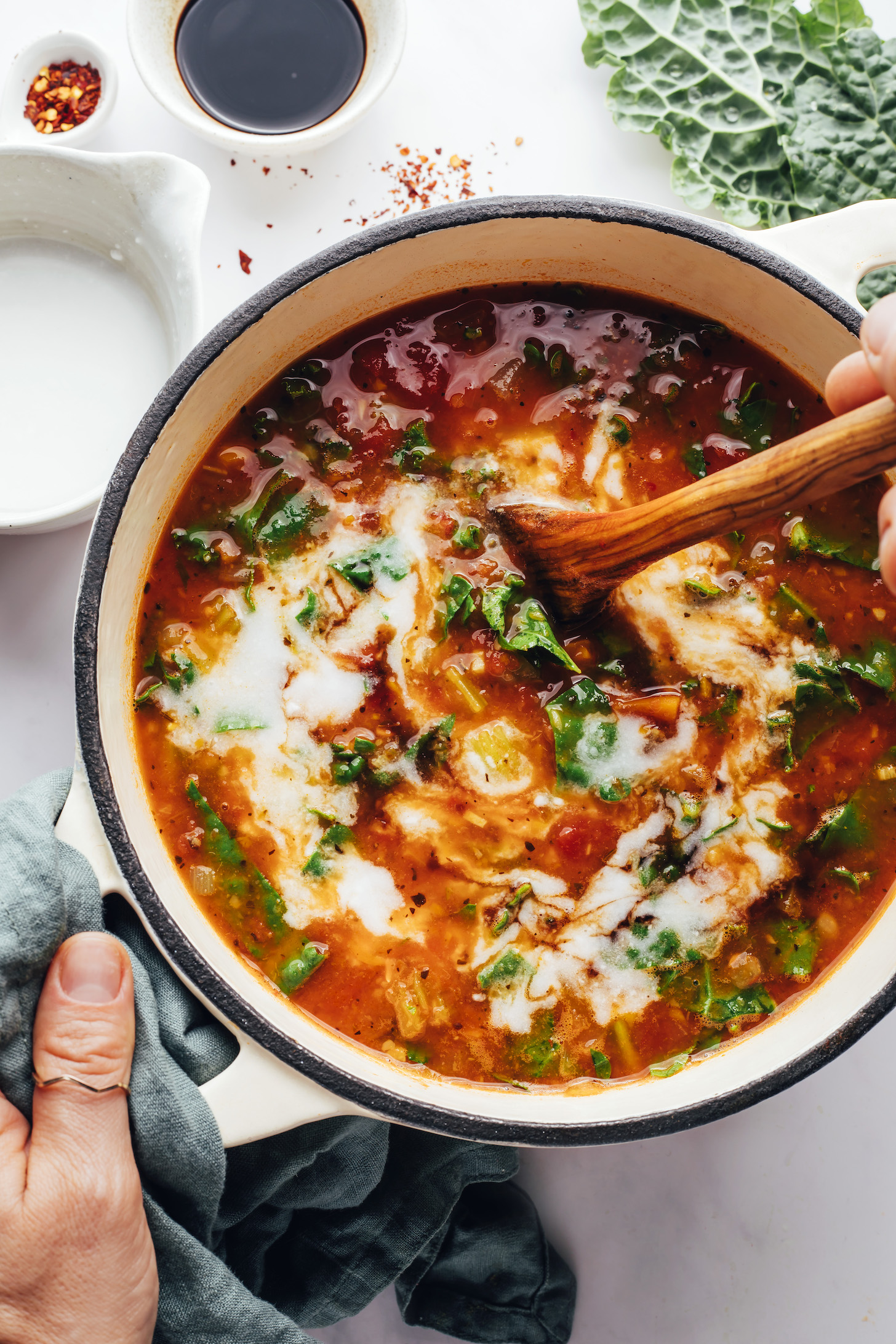 Stirring coconut milk into a vegan Tuscan soup with white beans and kale