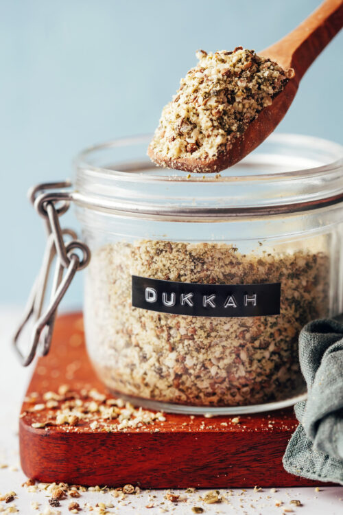 Spoonful of dukkah held above a jar of more of the spice mix
