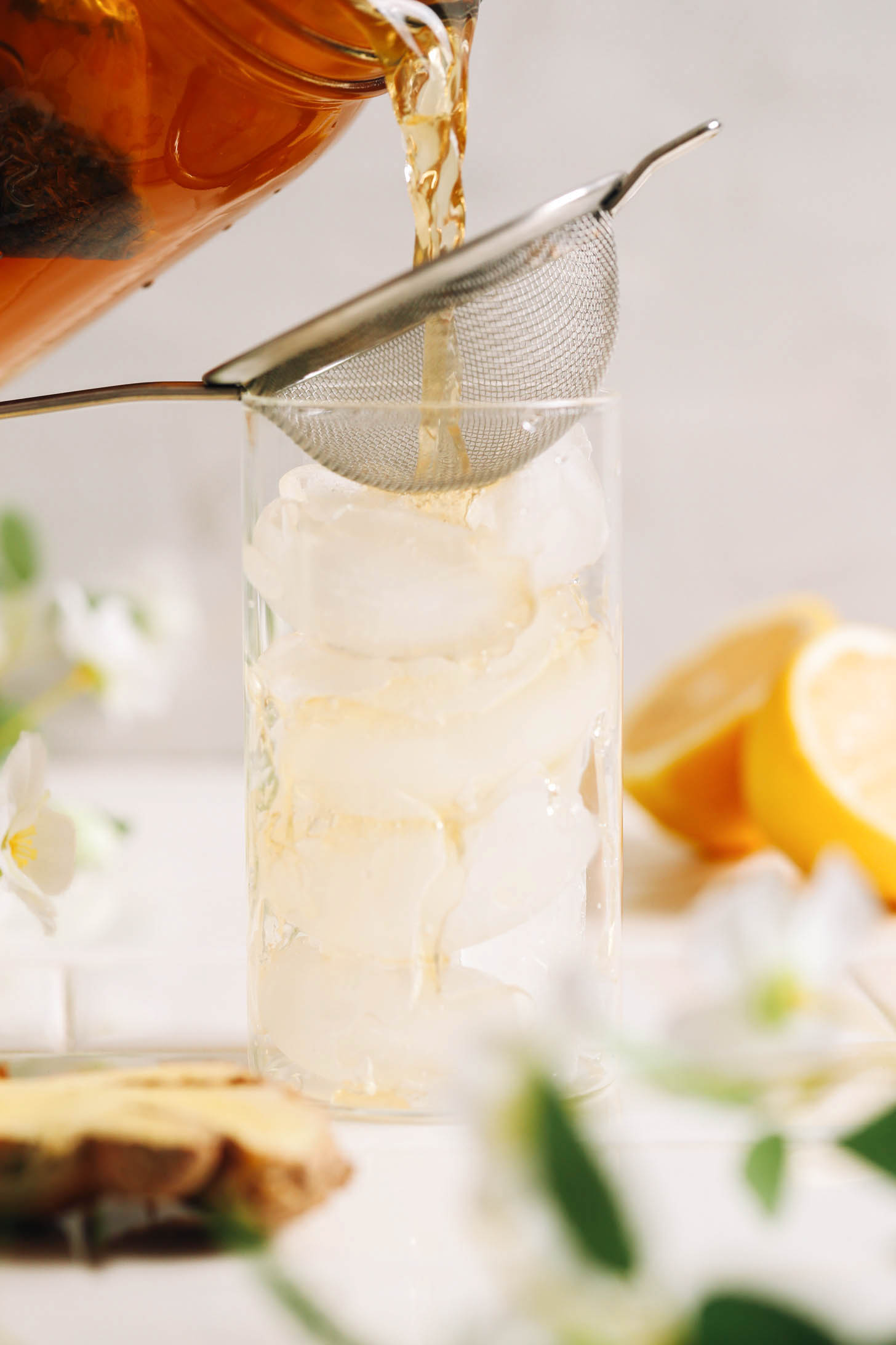 Pouring jasmine ginger tea through a fine mesh strainer into a glass of ice