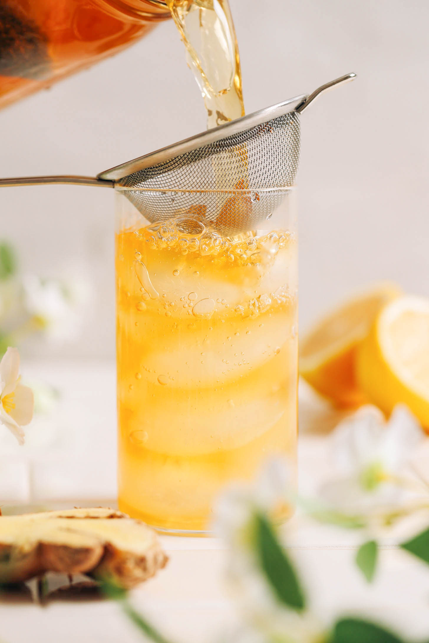 Mostly filled glass of jasmine ginger iced tea with a strainer of fresh ginger resting at the top