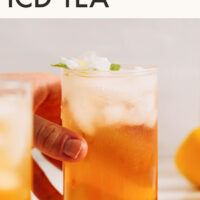 Hand reaching for a glass of jasmine ginger iced tea with text saying the recipe title above that