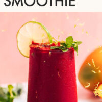 Glass of vegan and gluten-free vibrant mango beet smoothie with a fresh lime slice on the side