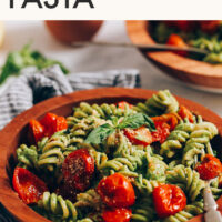 Bowl of creamy vegan pesto pasta with roasted tomatoes with text above it saying the recipe name
