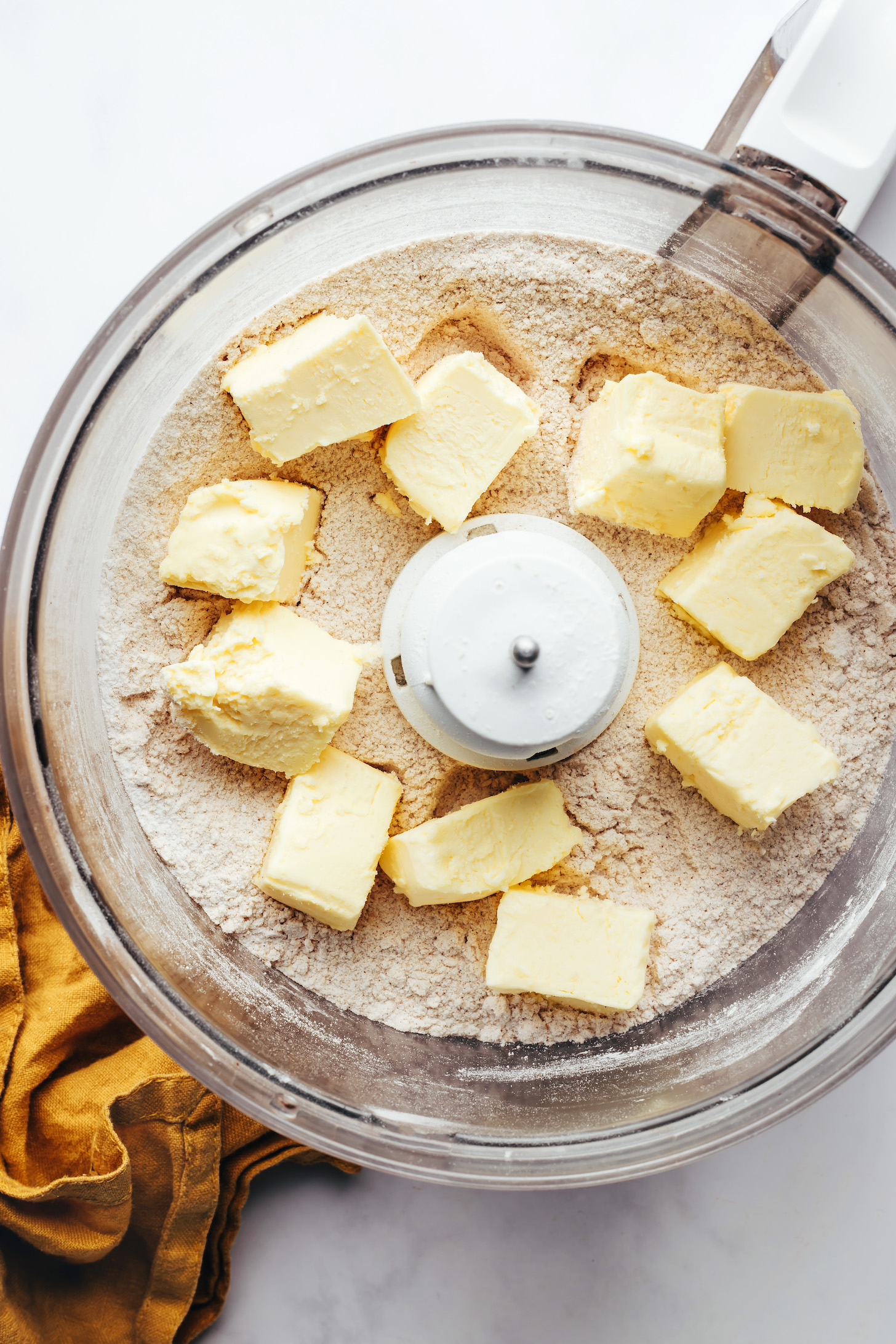 Food processor with cubes of vegan butter over blended flours