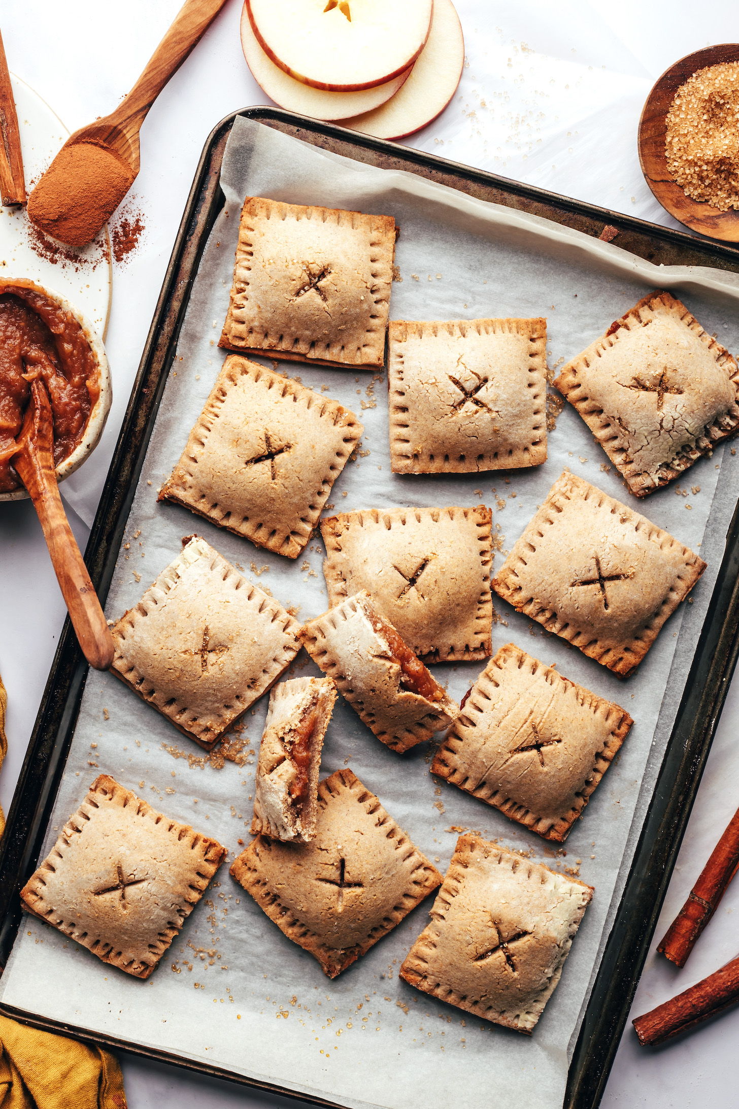 Apples, cinnamon, sugar, and apple butter around a baking sheet of homemade apple pop tarts