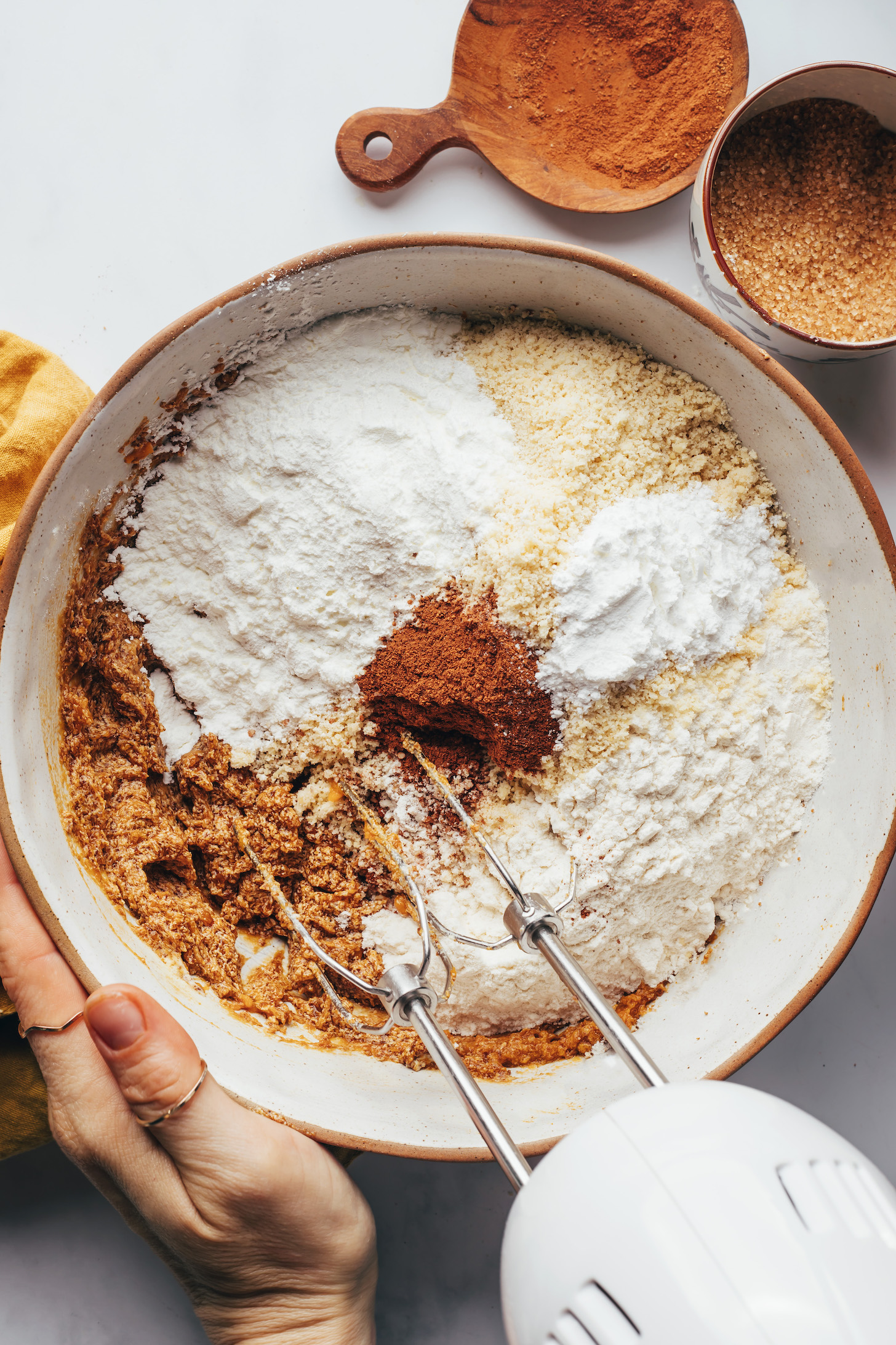 Gluten-free flours, cinnamon, baking powder, and salt at the top of a bowl of wet ingredients