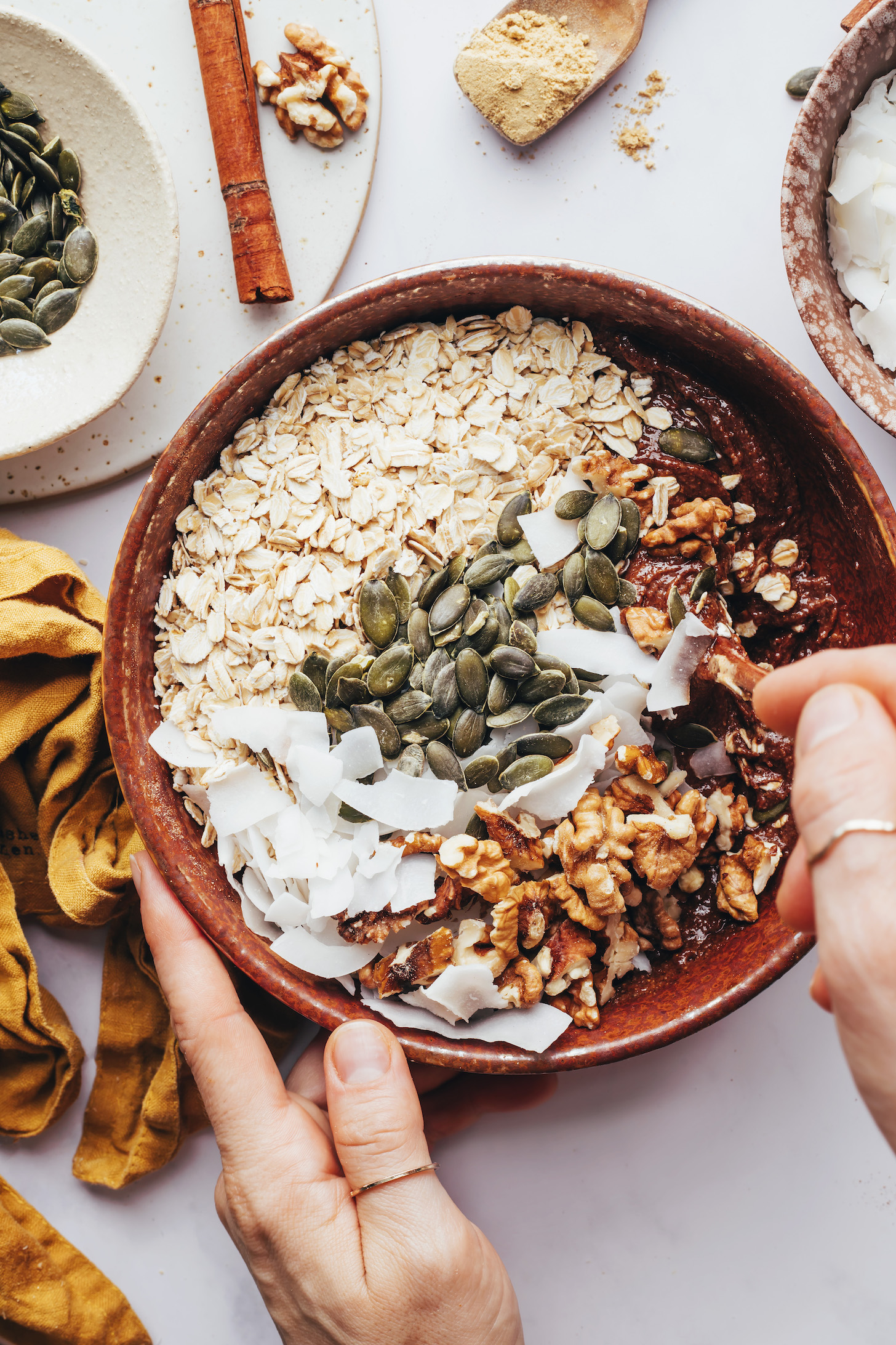 Stirring oats, pepitas, coconut flakes, walnuts, almond butter, and maple syrup in a bowl
