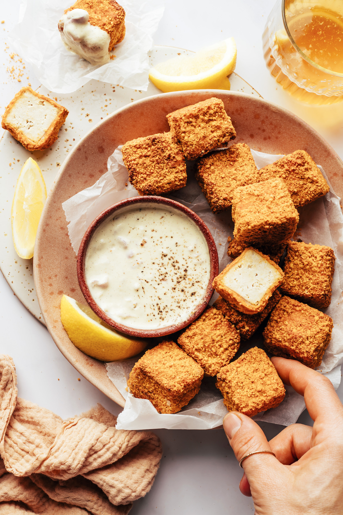 Hand reaching in to pick up a cashew-crusted tofu nugget from a plate