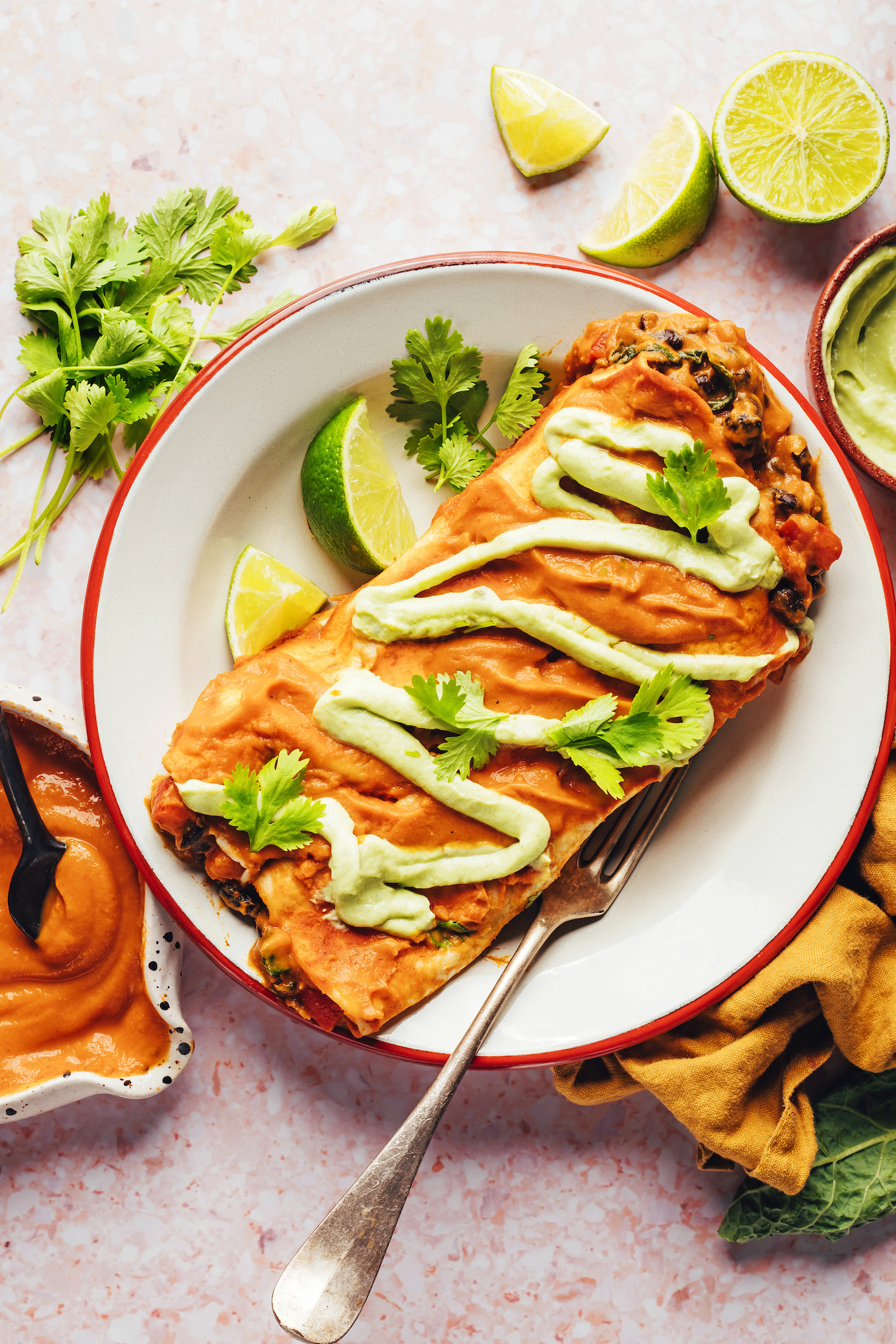 Plate of pumpkin black bean enchiladas topped with avocado crema and cilantro