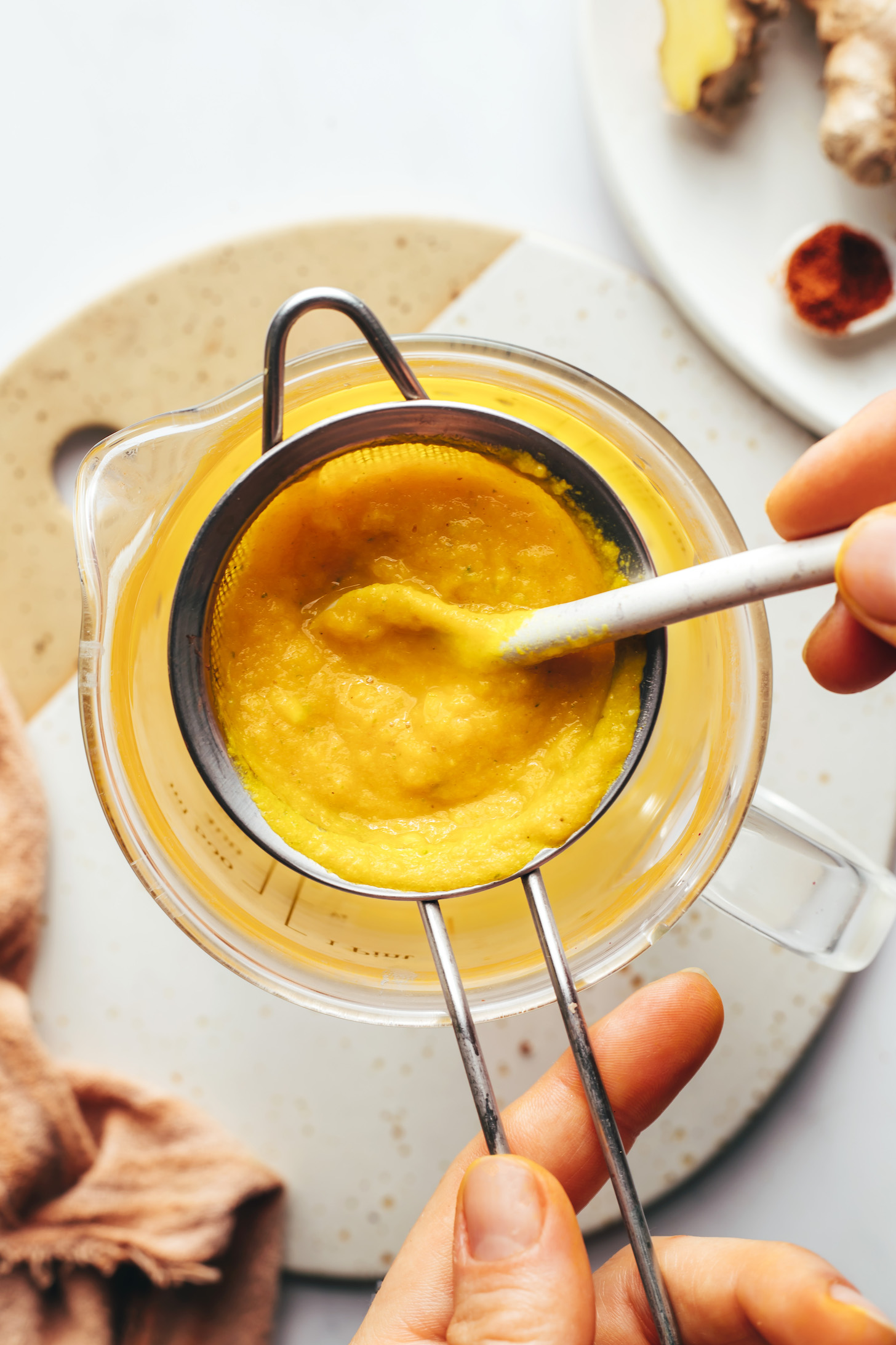 Holding a fine mesh strainer with fire cider pulp over a glass beaker