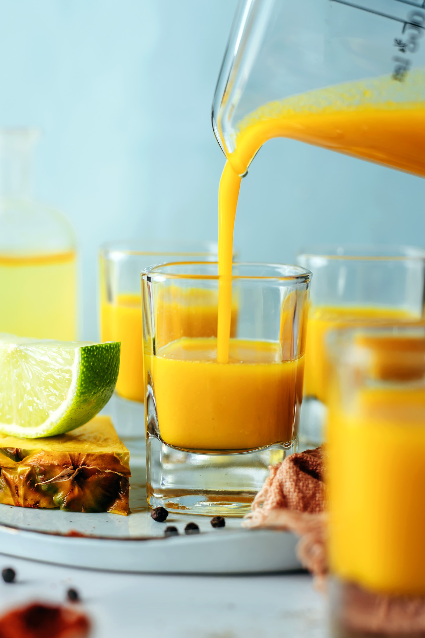 Pouring vibrant yellow-orange fire cider from a beaker into a shot glass