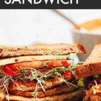 Sandwich on a plate with text above it reading chipotle hummus sandwich with smoky tempeh bacon