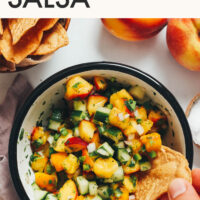 Dipping a tortilla chip into a bowl of peach cucumber salsa