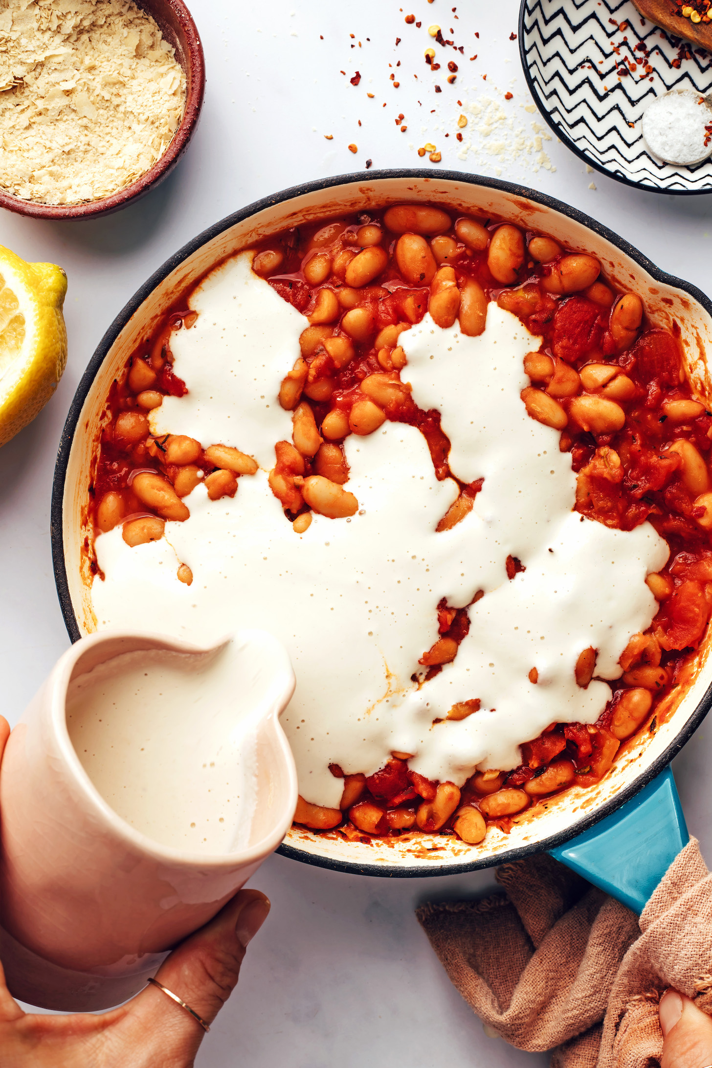 Pouring a creamy vegan sauce over a tomato bean mixture