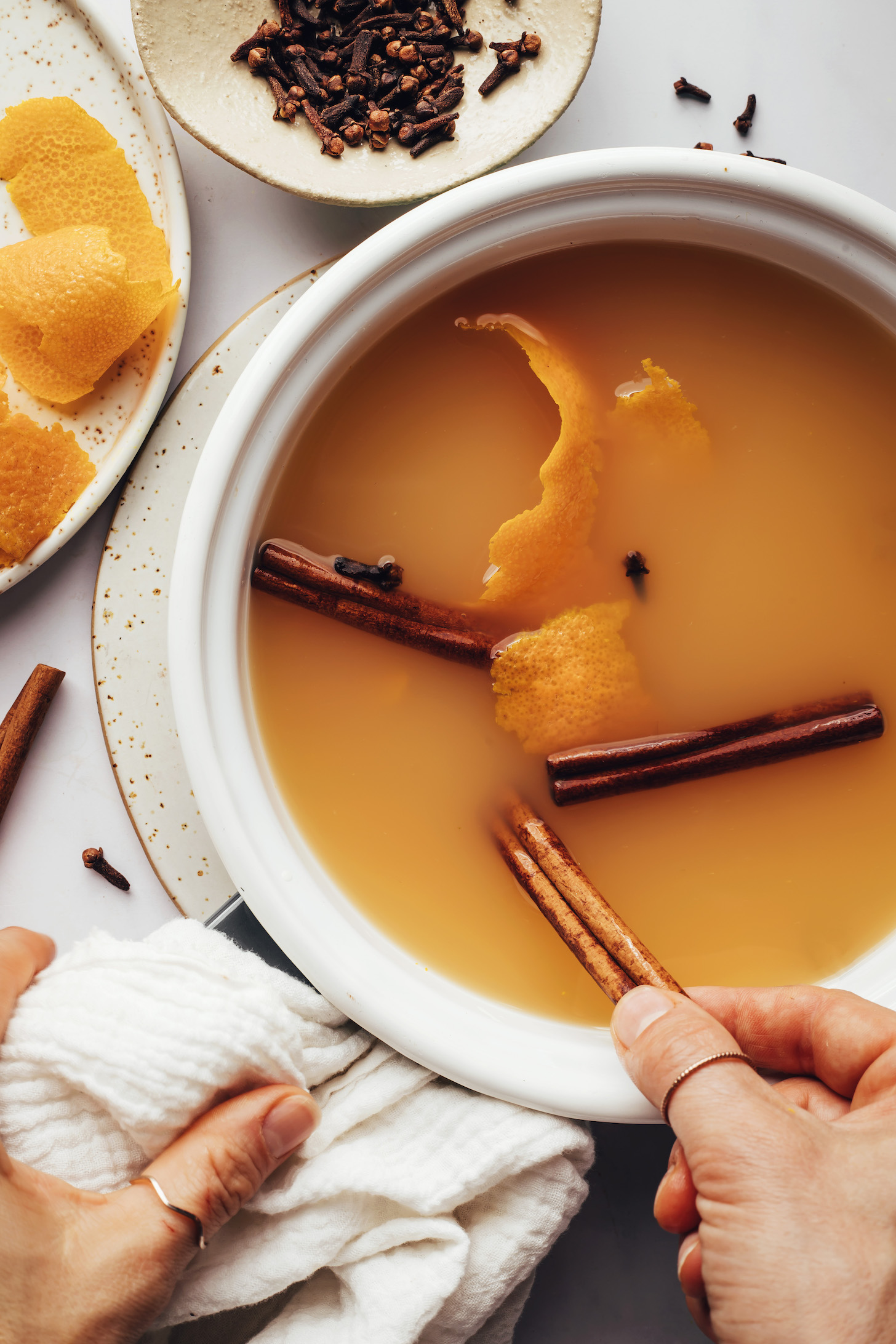 Adding cinnamon sticks to a saucepan of apple cider