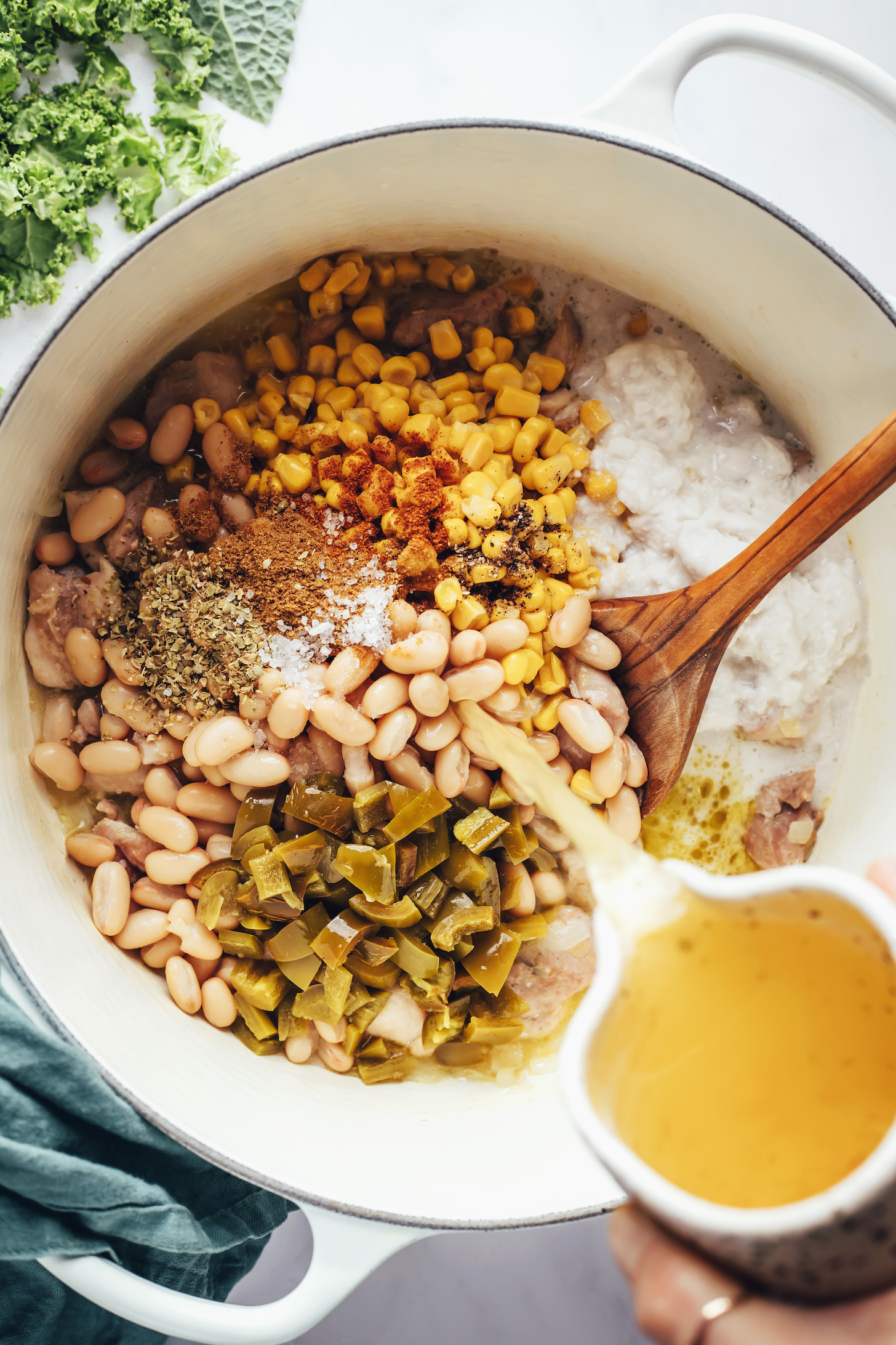 Pouring chicken broth over white beans, corn, hatch chiles, and spices