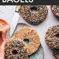 Hand reaching in to pick up the top half of a homemade gluten-free everything bagel